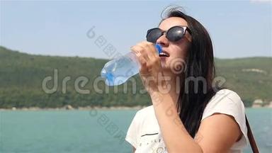 阳光明媚的夏日，年轻女子在山湖的<strong>背景</strong>下喝着<strong>纯净</strong>的水。
